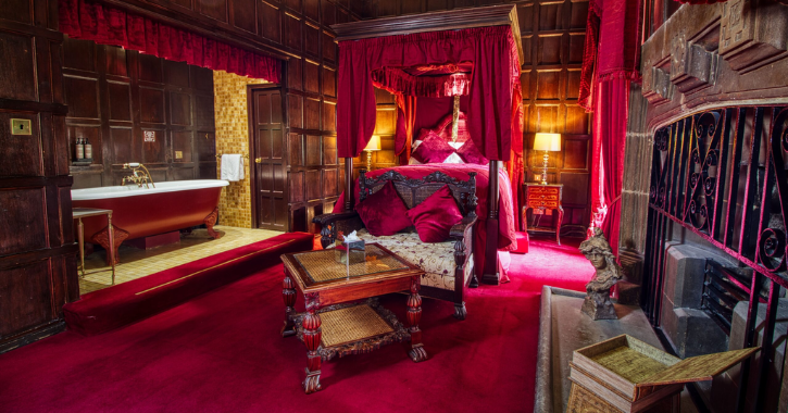 Bedroom suite inside Lumley Castle Hotel with dark wood panelling on walls and opulant red velvet furnishings.